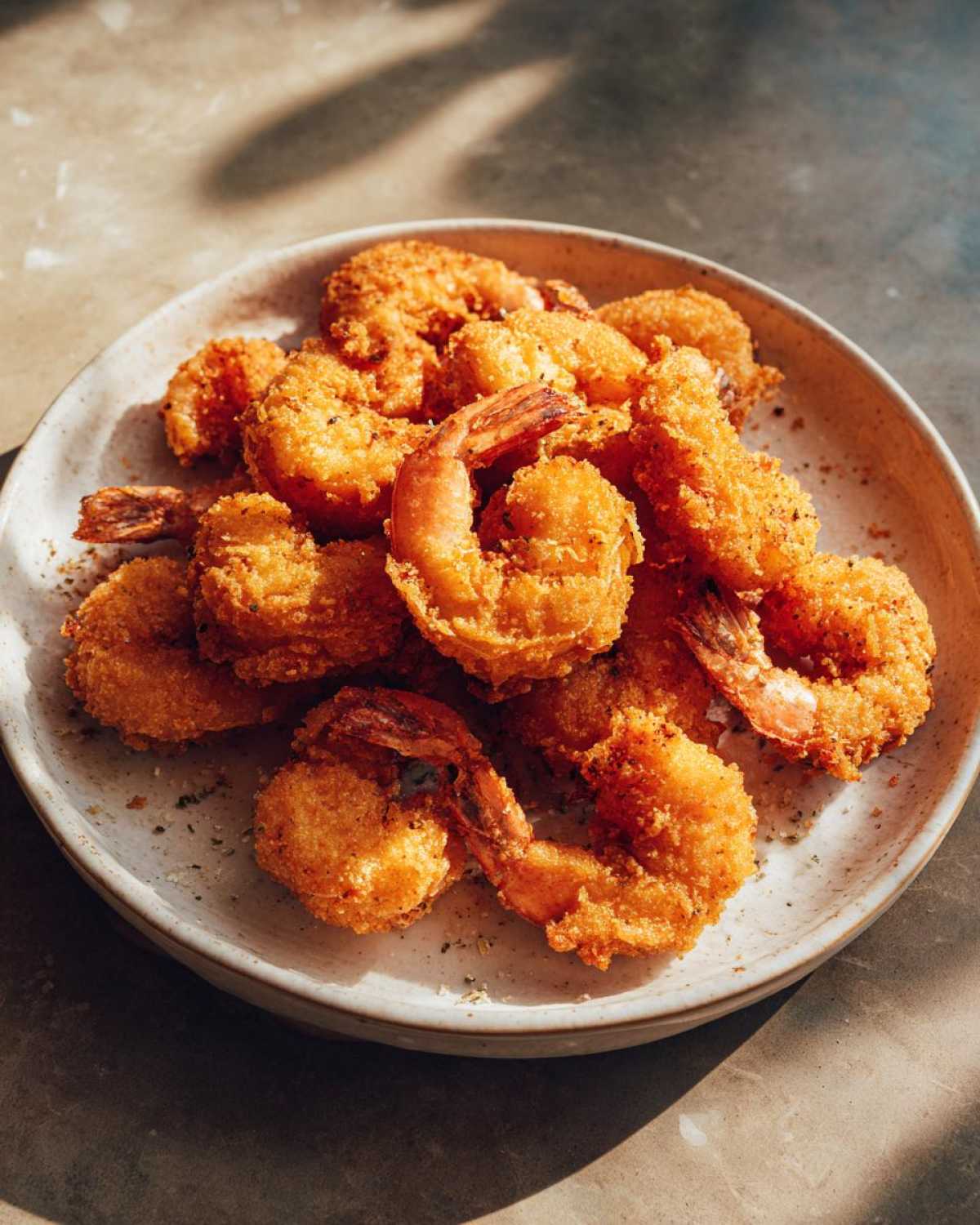 A pile of perfectly golden, crispy fried shrimp seasoned with herbs, served on a speckled ceramic plate.