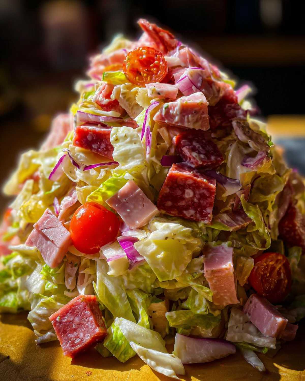 A towering mound of chopped lettuce, salami, ham, red onion, and cherry tomatoes tossed in dressing for a grinder salad.