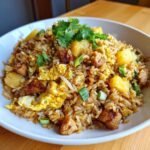 A close-up of a bowl filled with amazing pineapple fried rice, featuring chunks of pineapple, scrambled egg, and cilantro garnish.