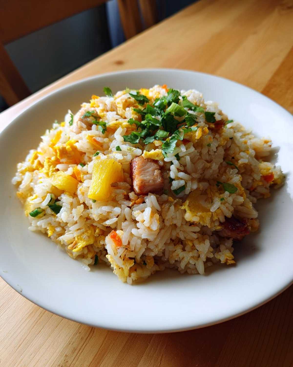A close-up of a white plate featuring a generous serving of pineapple fried rice, mixed with egg, pork pieces, and topped with fresh cilantro.