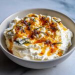 A bowl of creamy, whipped ricotta dip drizzled with amber honey and garnished with fresh rosemary sprigs.