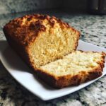 A golden-brown loaf of homemade soda bread, partially sliced, resting on a white plate.