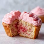 Close-up of a strawberry cupcake cut in half showing moist cake and pink strawberry frosting.