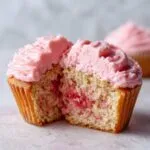 Close-up of a strawberry cupcake cut in half showing moist cake and pink strawberry frosting.
