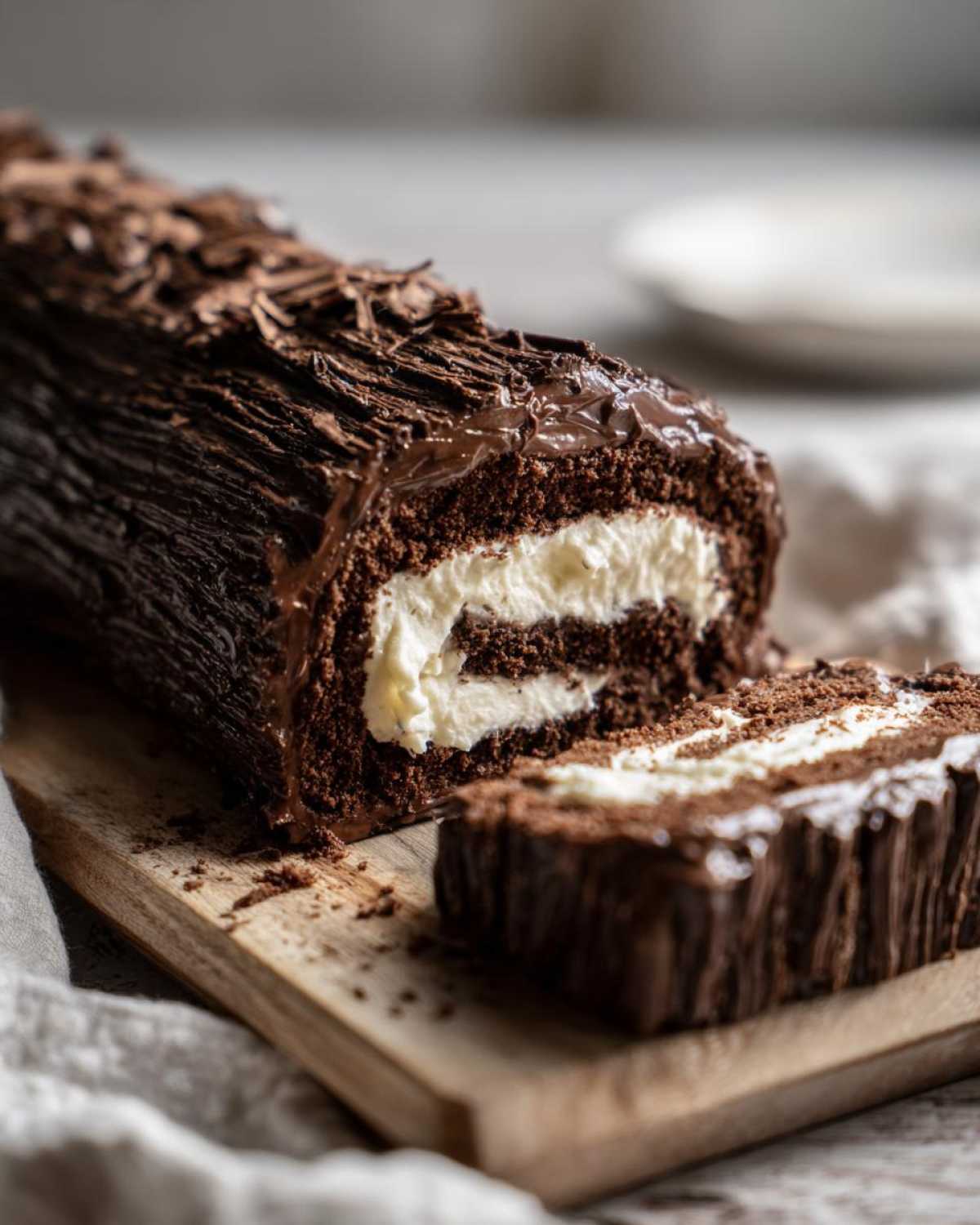 A rich chocolate yule log cake, partially sliced, revealing a thick white cream filling.