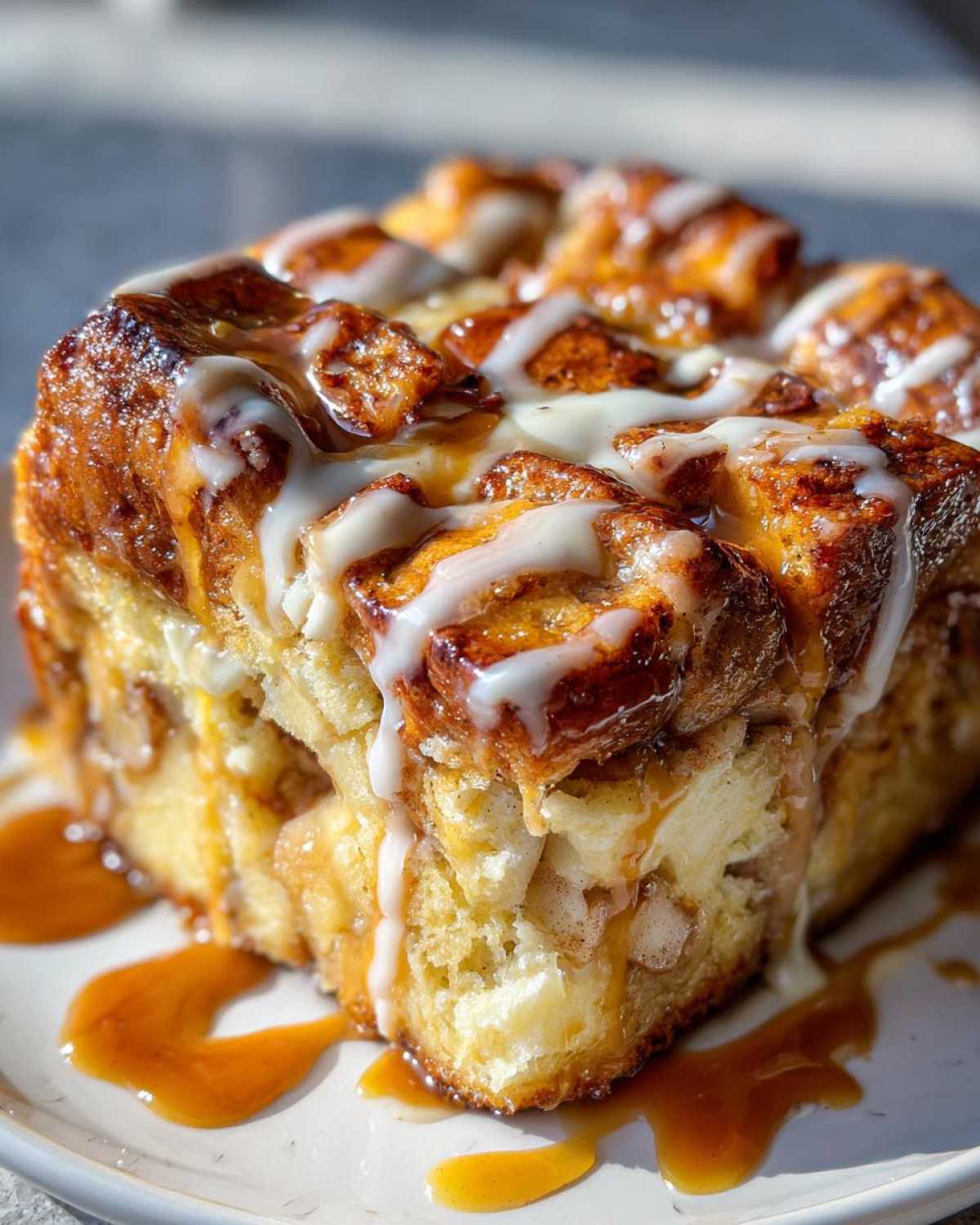 Close-up of a moist slice of apple bread pudding topped with white glaze and caramel sauce.