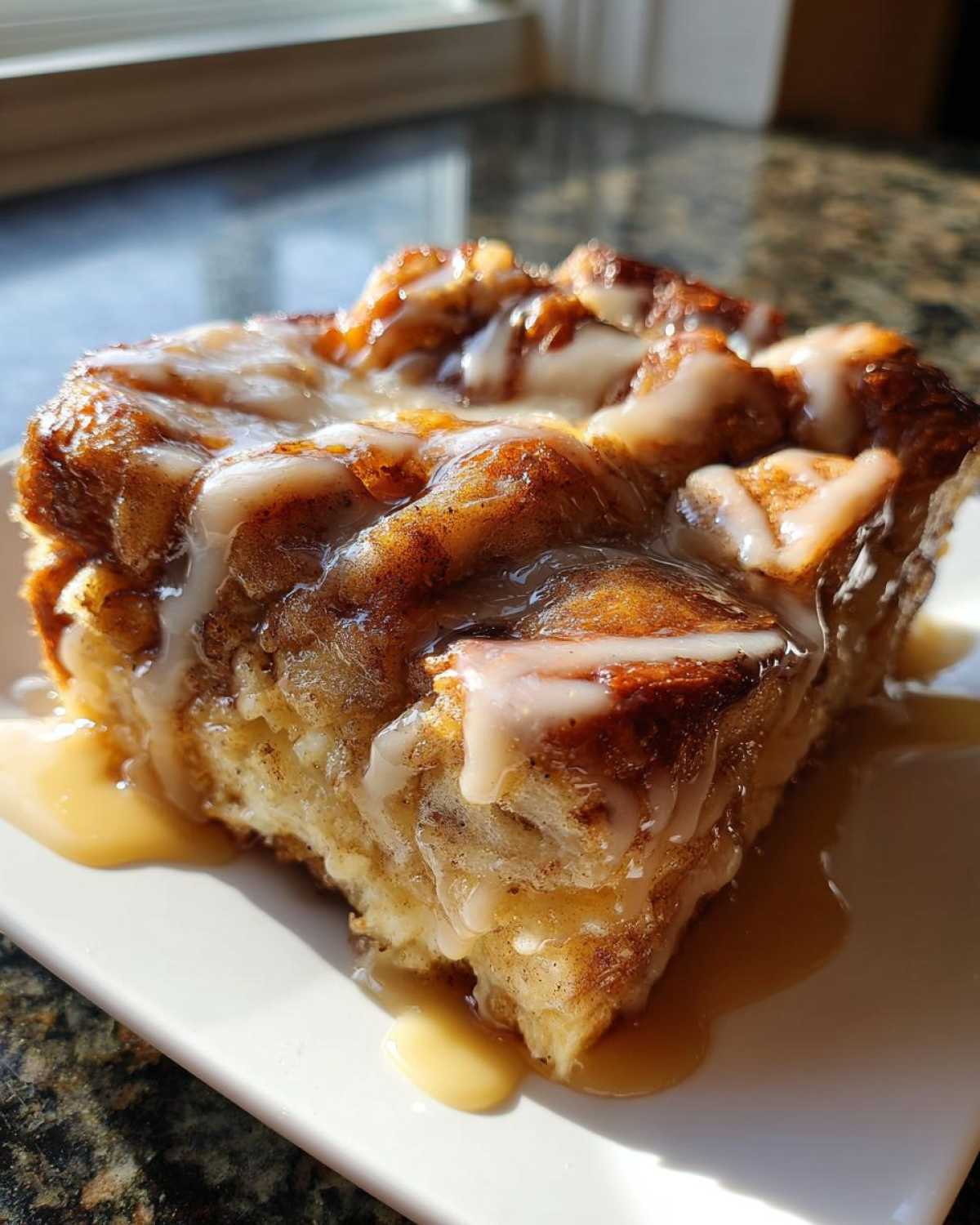 A close-up of a moist slice of apple bread pudding topped with white icing and caramel sauce.