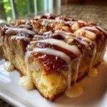 A close-up of a moist slice of apple bread pudding topped with a rich caramel glaze and drizzled with white icing.