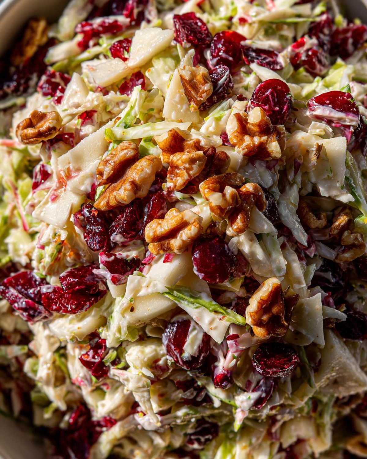 A close-up, vibrant shot of apple cranberry coleslaw mixed with creamy dressing, dried cranberries, and crunchy walnuts.