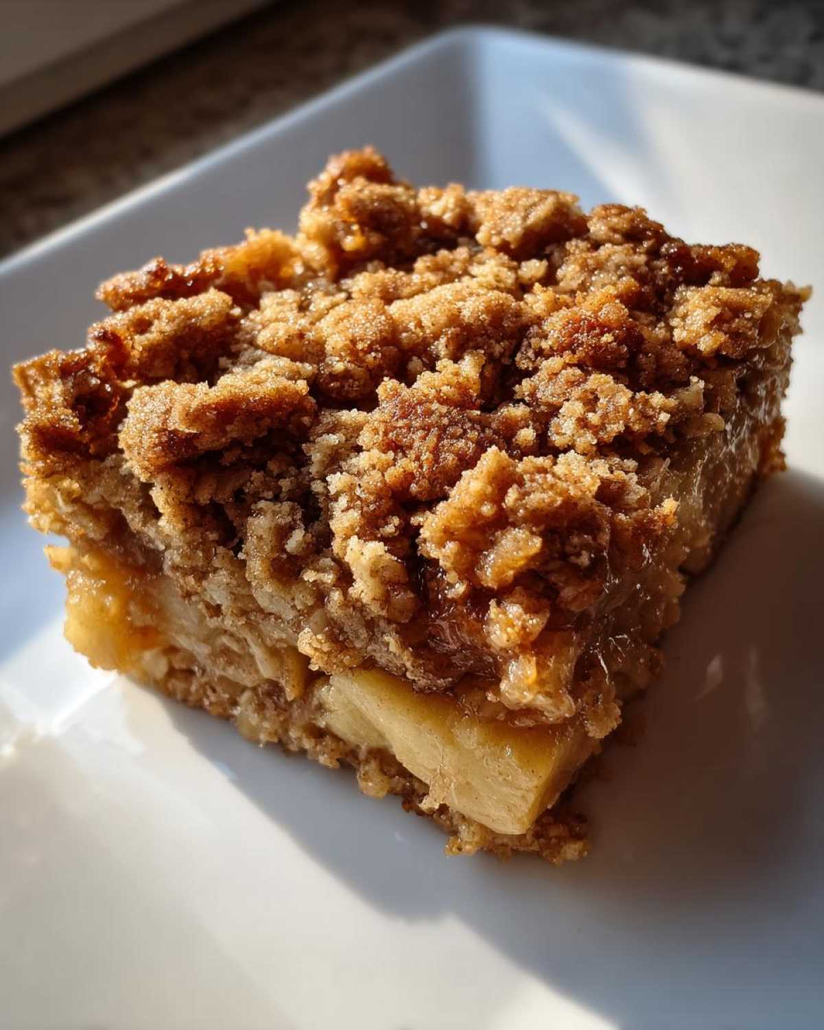 Close-up of a square slice of apple baked oatmeal with a thick, golden brown streusel crumb topping.