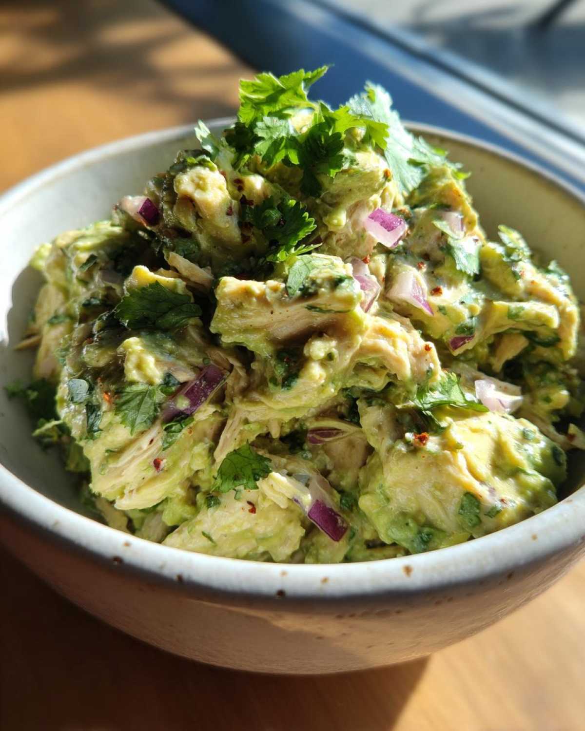 Close-up of creamy avocado chicken salad mixed with red onion and topped with fresh cilantro.