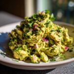 A mound of creamy avocado chicken salad mixed with chunks of avocado, red onion, and cilantro, served on a light plate.