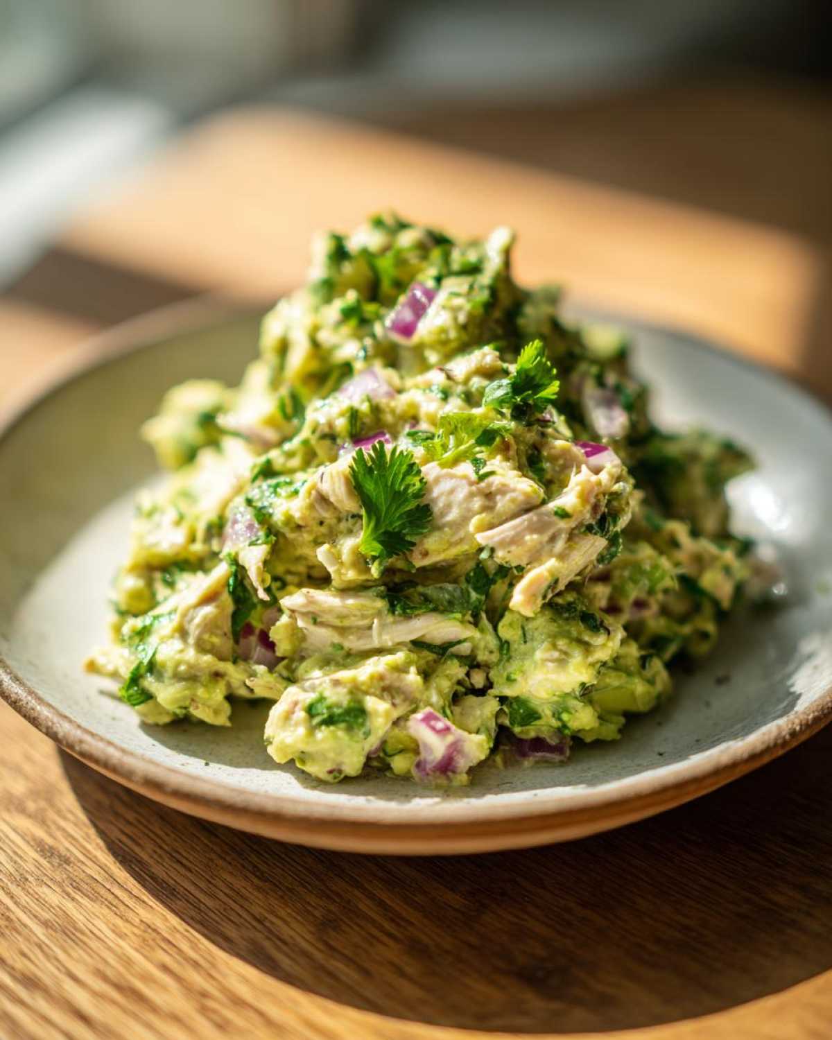 A mound of creamy avocado chicken salad mixed with chunks of red onion and fresh cilantro on a small plate.