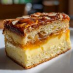 A close-up slice of bee sting cake showing three distinct layers: cake base, creamy filling, and caramelized almond topping.