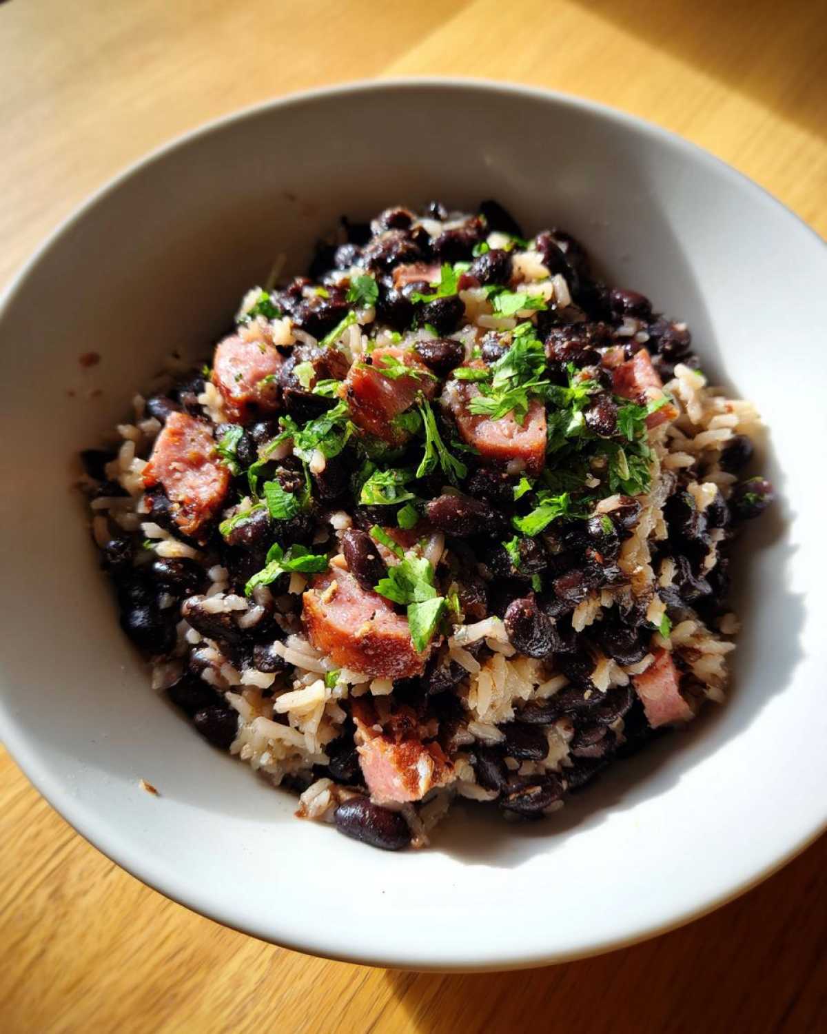 A bowl filled with hearty black beans and rice mixed with chunks of sausage and topped with fresh cilantro.