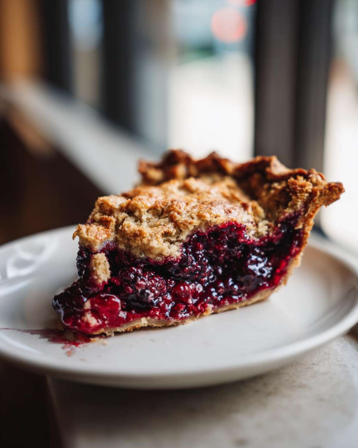 Close-up of a juicy slice of blackberry pie with a golden crumb topping on a white plate.