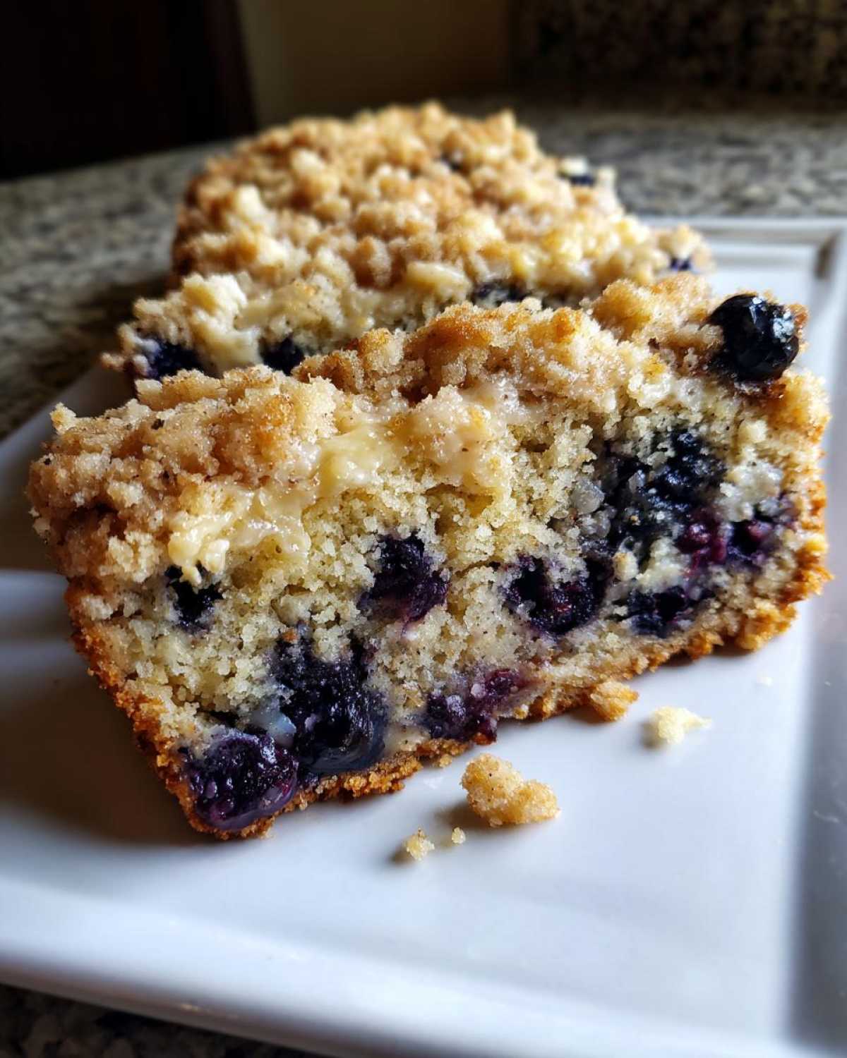 Close-up of a moist slice of blueberry banana bread featuring visible blueberries and a sweet crumb topping.