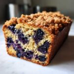 A close-up cross-section of moist blueberry banana bread featuring visible blueberries and a crumbly streusel topping.
