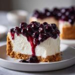 A perfect slice of creamy blueberry cheesecake topped with rich blueberry compote dripping down the side.