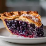 Close-up of a thick slice of blueberry pie recipe showing juicy filling and sugared crust.