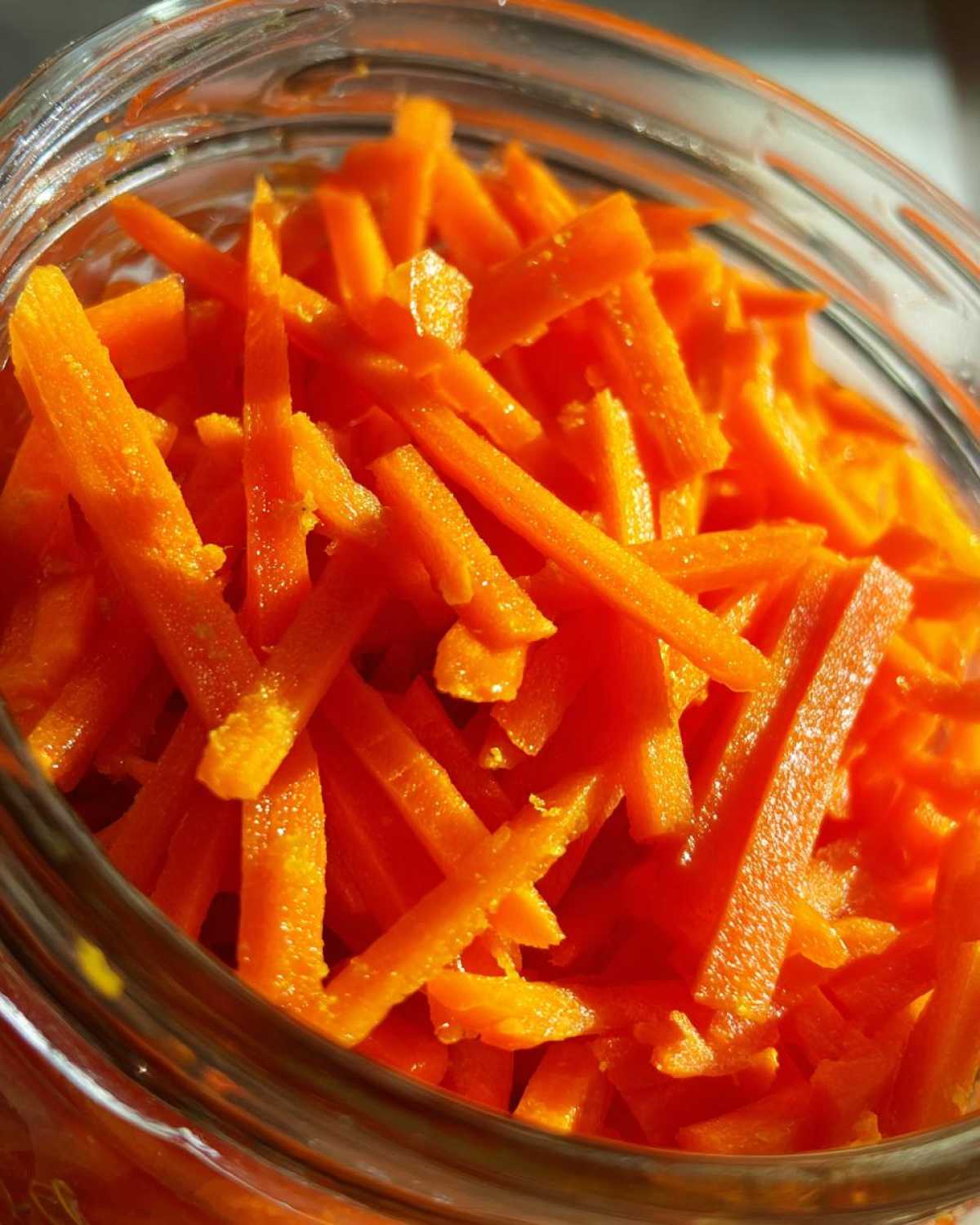 Close-up view of vibrant, julienned pickled carrots packed tightly inside a clear glass jar.