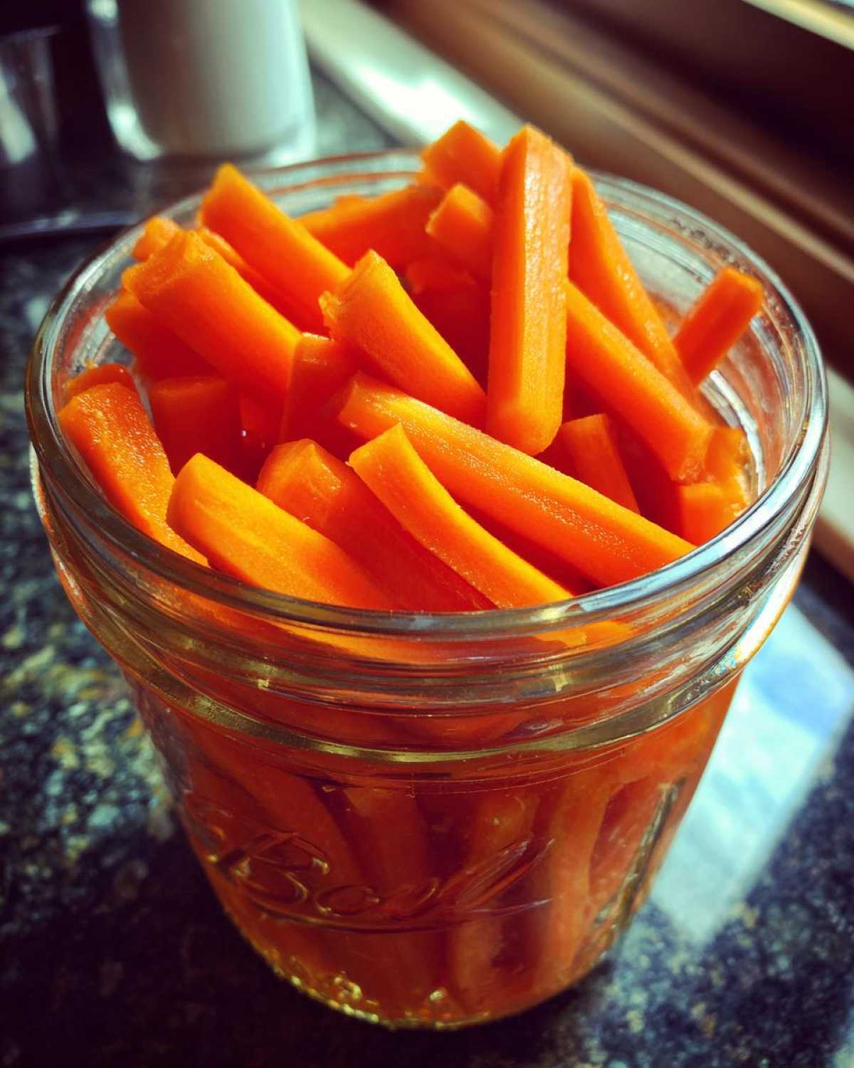 Close-up of bright orange, stick-cut pickled carrots filling a clear Ball mason jar.