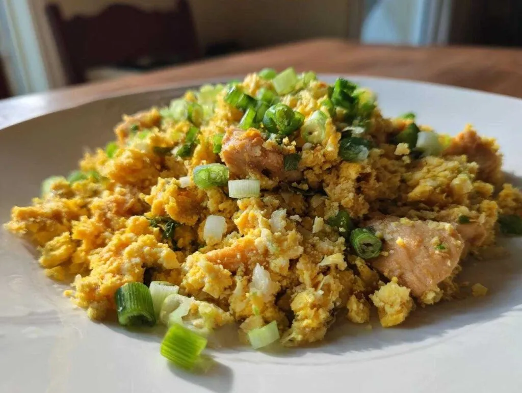 A close-up of bright yellow cauliflower fried rice topped generously with chopped green onions on a white plate.