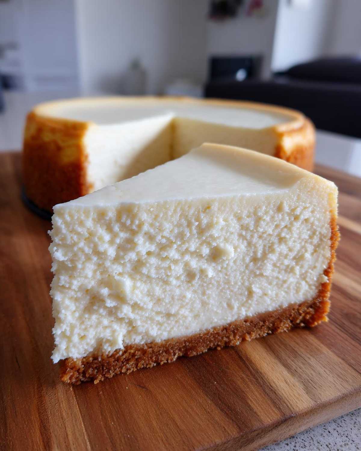 A close-up slice of creamy baked cheesecake with a graham cracker crust, next to the rest of the cheesecake recipe.