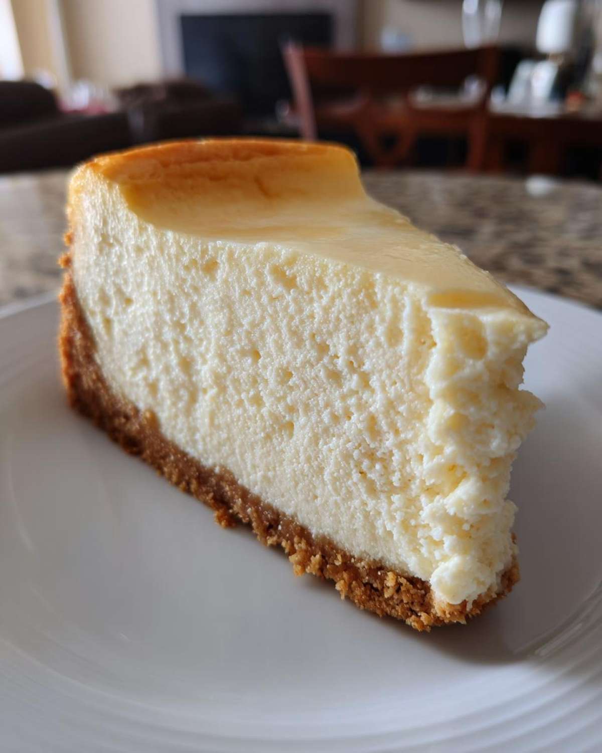 A thick, creamy slice of baked cheesecake with a golden top and graham cracker crust, ready to eat from our cheesecake recipe.