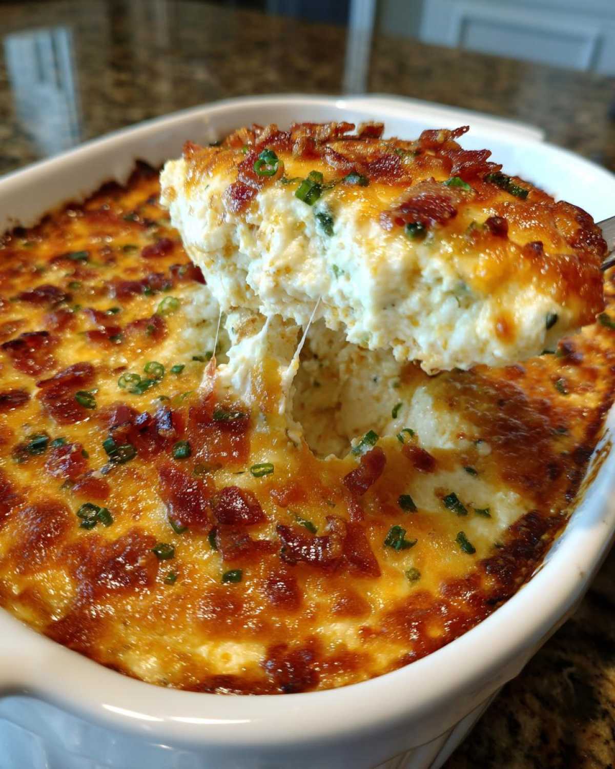 A spoonful of hot, cheesy bacon popper dip is lifted from a white baking dish, showing a cheese pull.