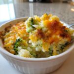 A spoonful of creamy, cheesy broccoli rice being lifted from a white ramekin dish.