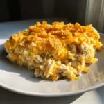 A serving of cheesy chicken and rice casserole topped with melted cheddar and crunchy cornflakes on a light plate.