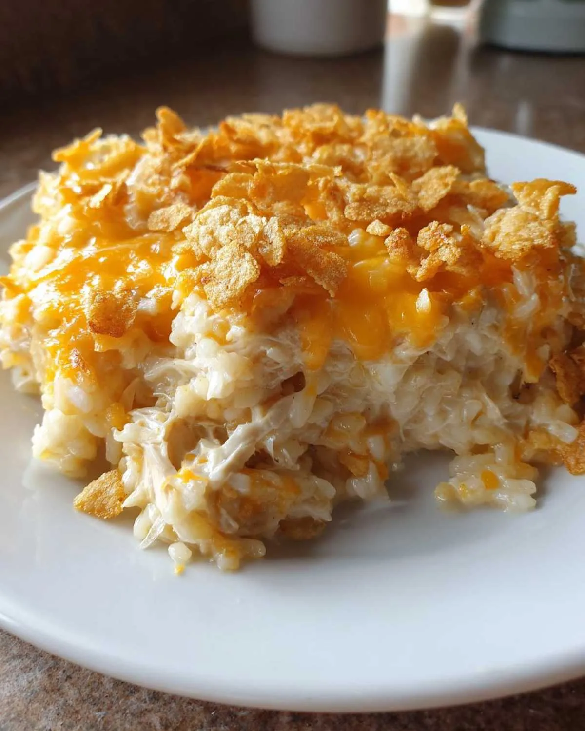 A close-up serving of cheesy chicken and rice casserole topped with melted cheddar and crushed cornflakes.