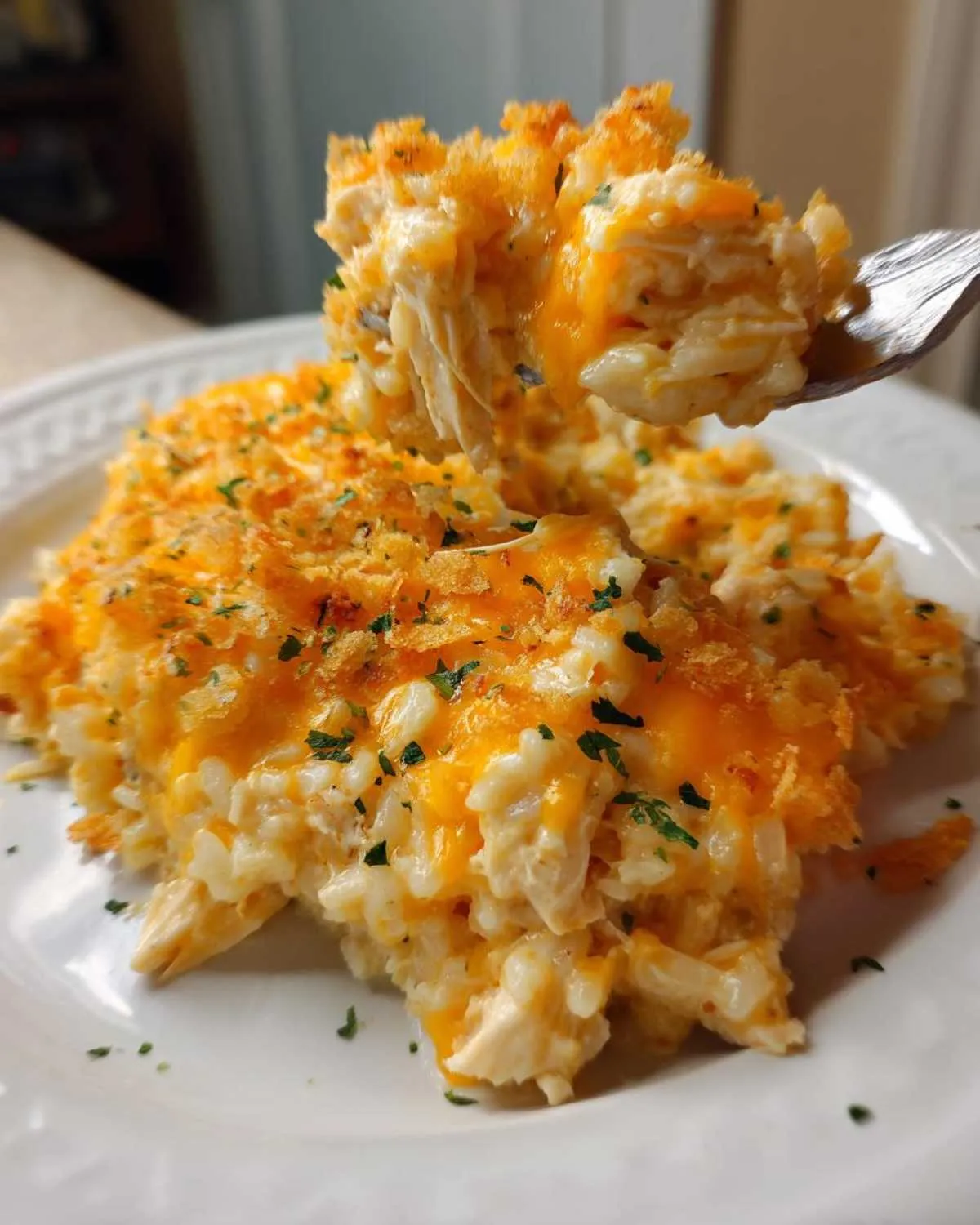 A fork lifting a scoop of creamy, cheesy chicken and rice topped with melted cheddar and crispy breadcrumbs.
