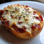 A close-up of a single, freshly baked pizza bagel half topped with melted mozzarella cheese and herbs.