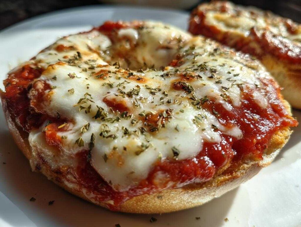 A close-up, appetizing shot of a freshly baked pizza bagel topped with melted mozzarella, tomato sauce, and dried herbs.