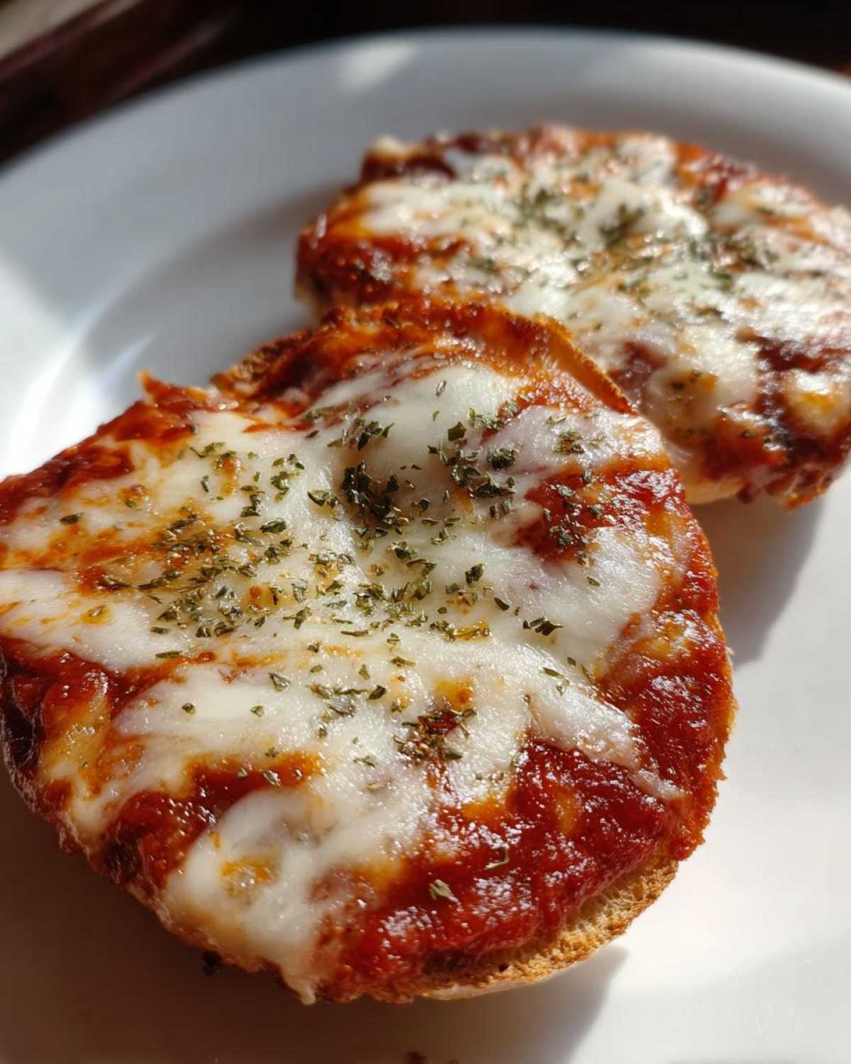 Two halves of freshly made pizza bagels topped with melted mozzarella cheese, rich tomato sauce, and dried herbs.
