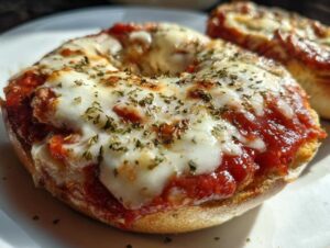 A close-up, appetizing shot of a freshly baked pizza bagel topped with melted mozzarella, tomato sauce, and dried herbs.