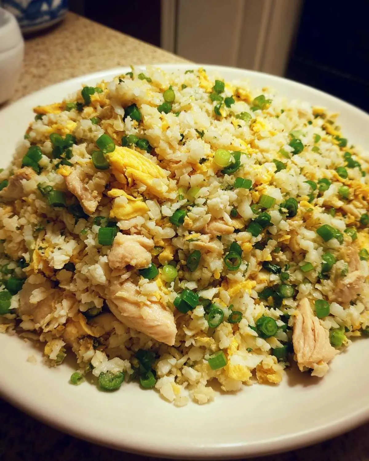 A generous serving of chicken cauliflower fried rice topped with scrambled egg pieces and bright green chopped scallions.