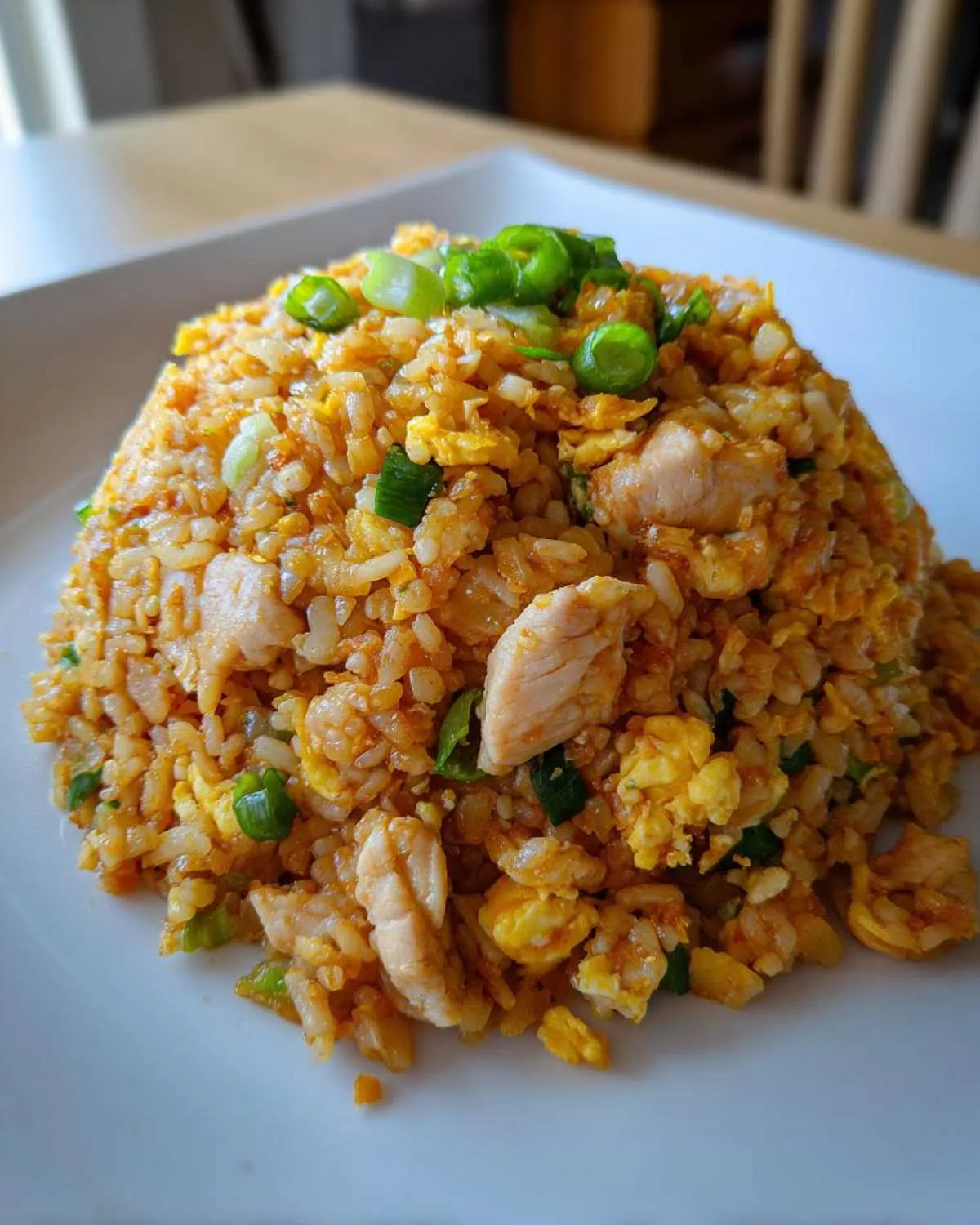 A mound of flavorful chicken cauliflower fried rice garnished with fresh green onions on a white plate.