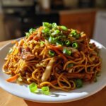 A heaping portion of savory chicken chow mein recipe, topped generously with sliced green onions, served on a white plate.