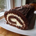 A cross-section slice of a rich chocolate yule log cake showing the dark sponge rolled with white cream filling.