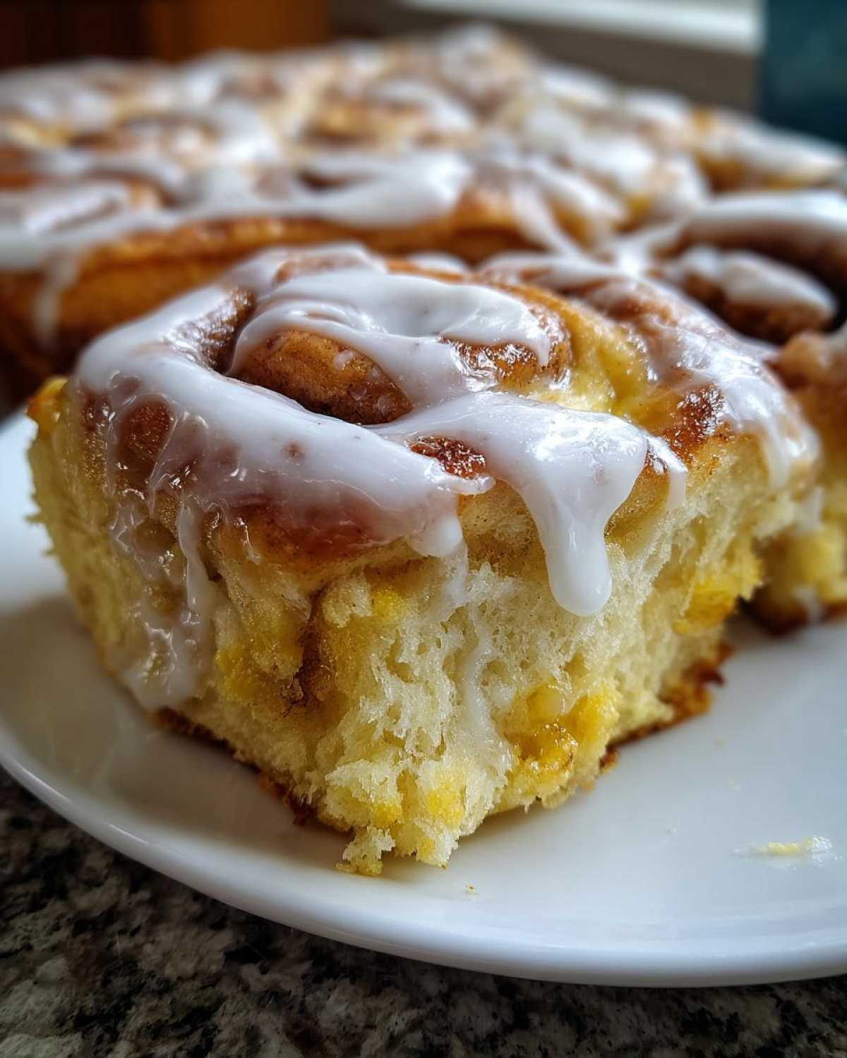 A close-up of a soft, glazed piece of cinnamon roll french toast on a white plate.