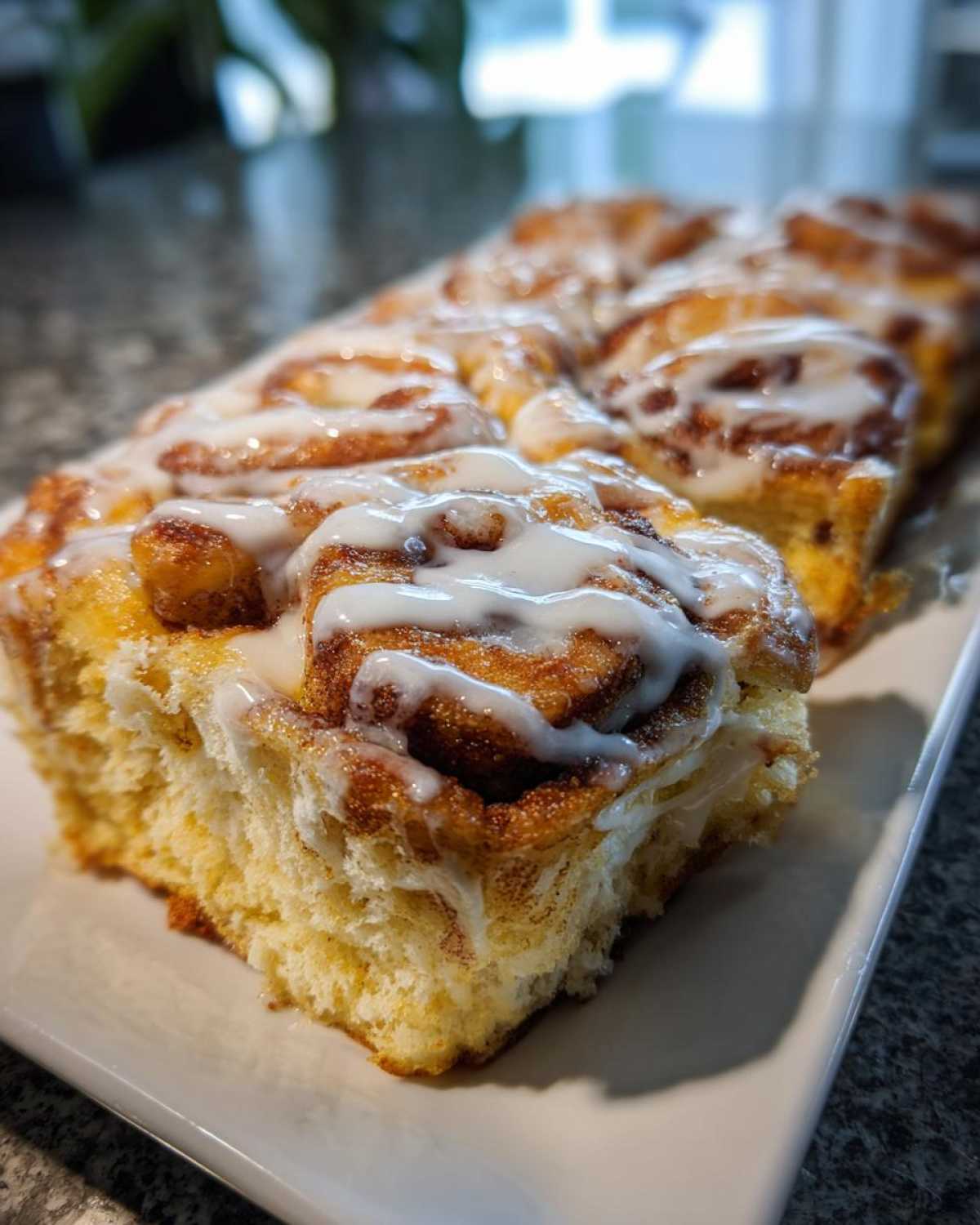 A close-up of a serving of cinnamon roll french toast, showing the fluffy interior and thick white icing drizzle.