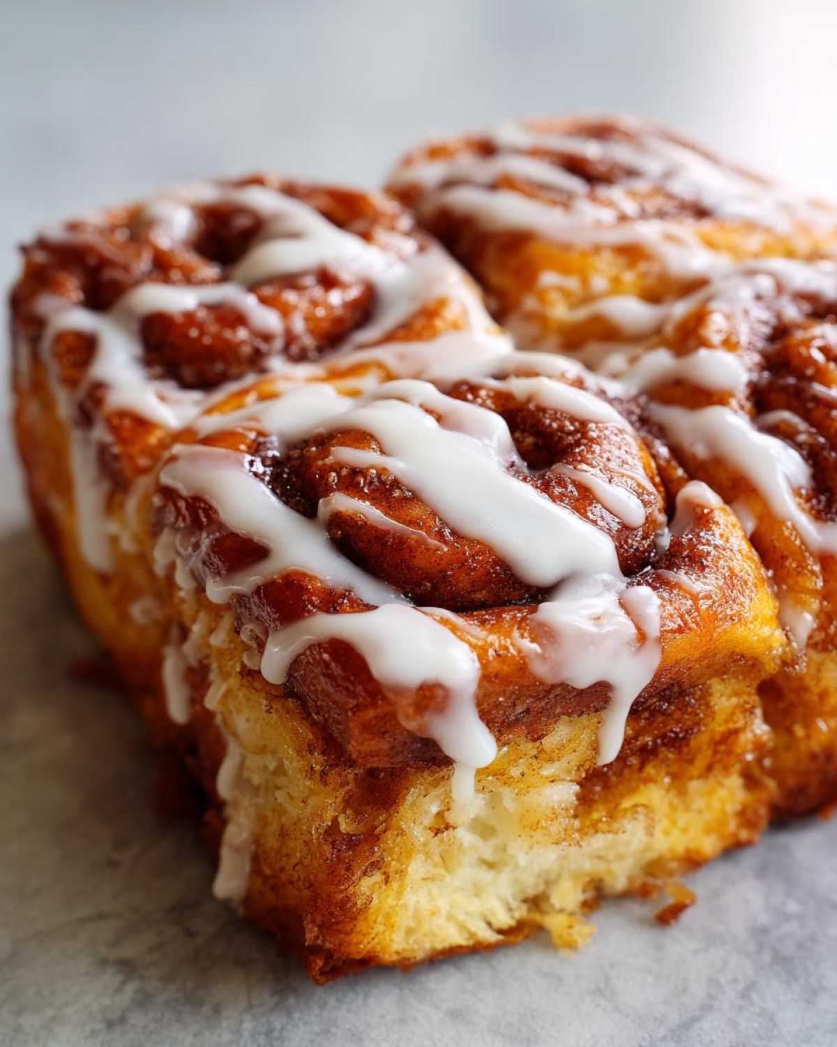Close-up of baked cinnamon rolls, likely used for cinnamon roll french toast, drizzled heavily with white icing.