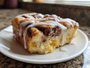 A single serving of cinnamon roll french toast, drizzled heavily with white icing, resting on a small white plate.