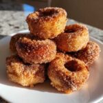 A close-up stack of freshly made, golden brown mini donuts coated heavily in cinnamon sugar.