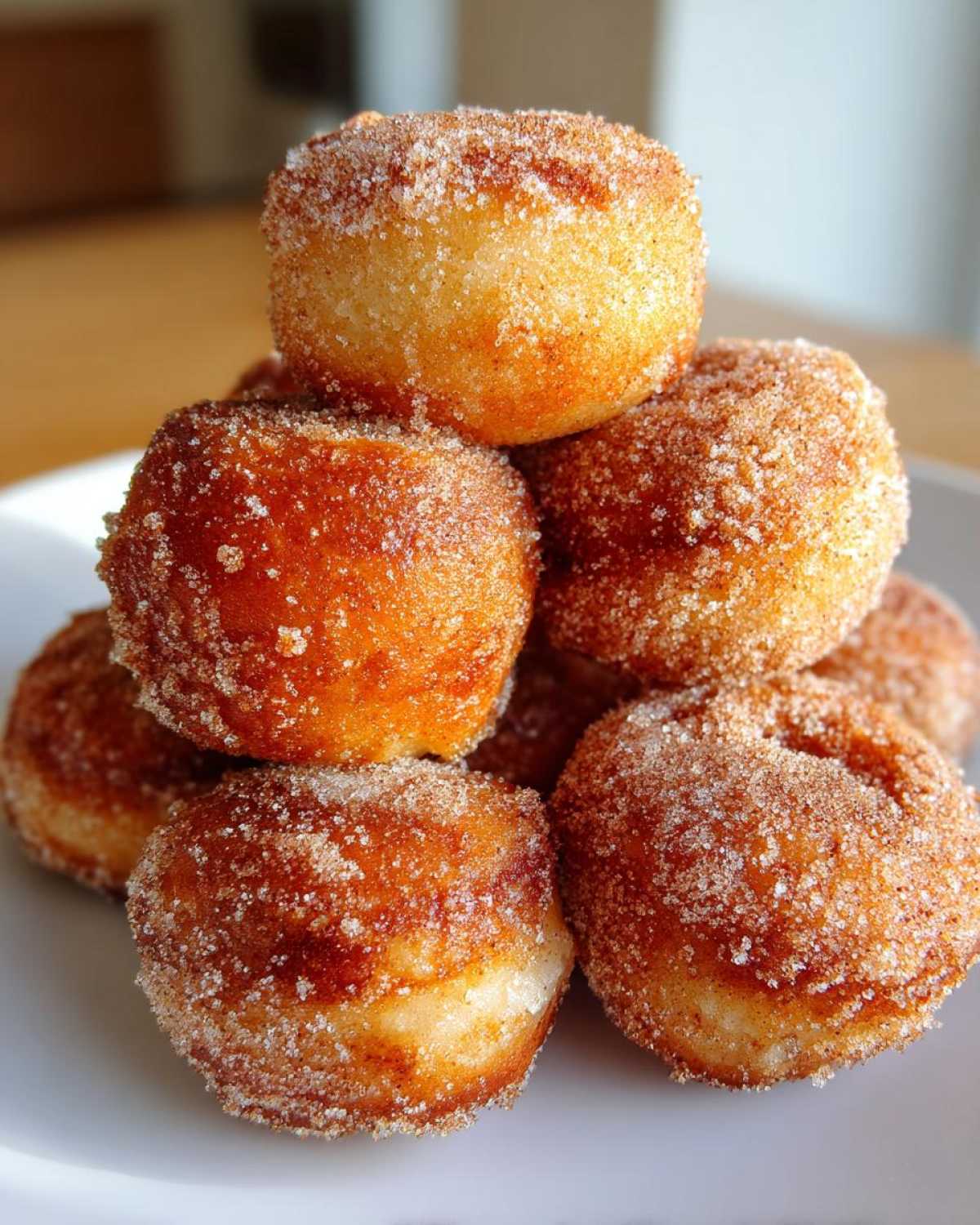 Close-up of a stack of golden brown, freshly fried mini donuts coated in cinnamon sugar.