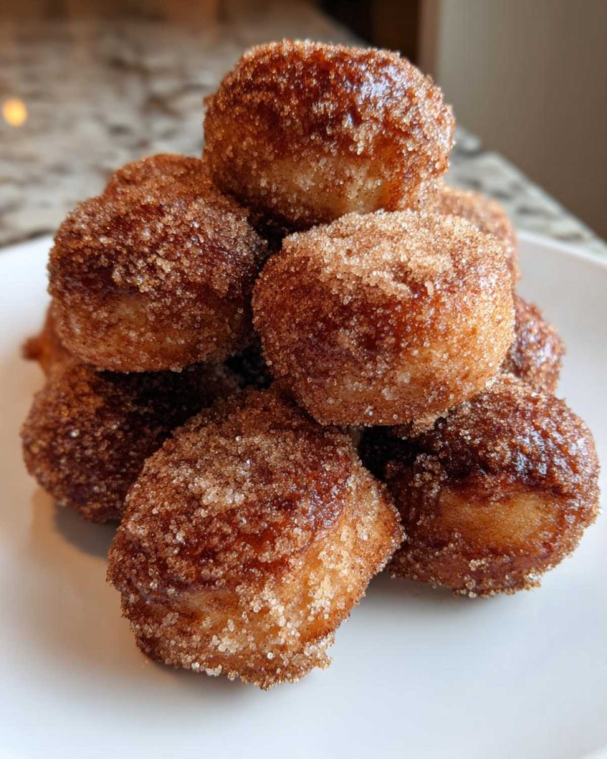 A close-up stack of freshly made, golden brown mini donuts coated heavily in cinnamon sugar.