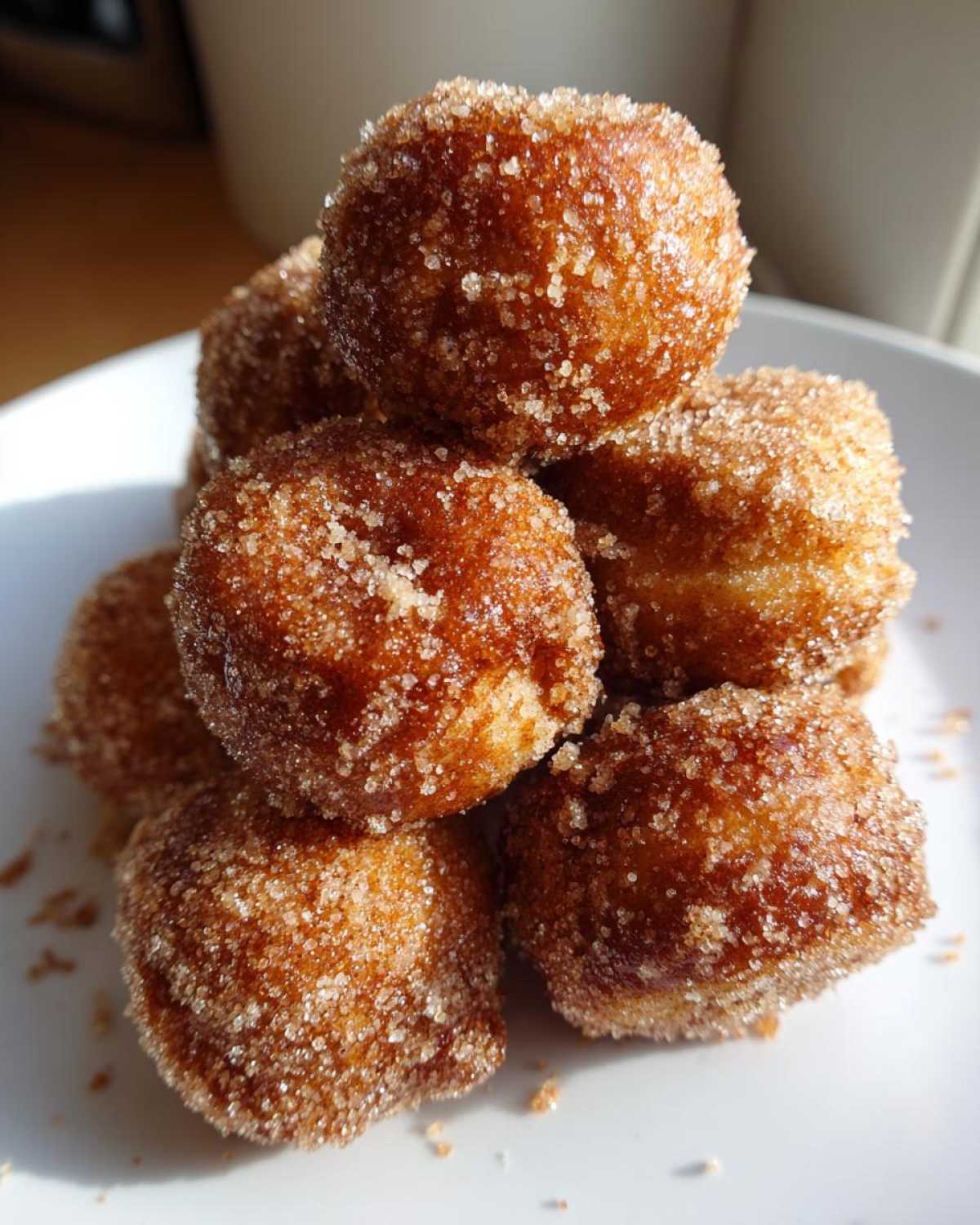 Close-up of a stack of freshly made, golden brown mini donuts heavily coated in sparkling cinnamon sugar.